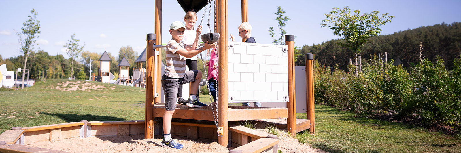 Children play on a playground unit which is situated on top of sand so they can use pulleys to pull sand up to the top.